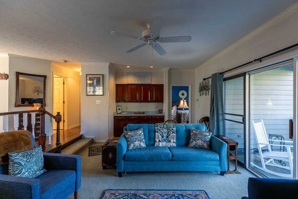 A comfortable living space featuring a blue couch, wooden furniture, and sliding glass doors leading to a covered patio. The arrangement invites lounging, reading, or chatting, while the sliding doors provide a seamless connection to the outdoor space.