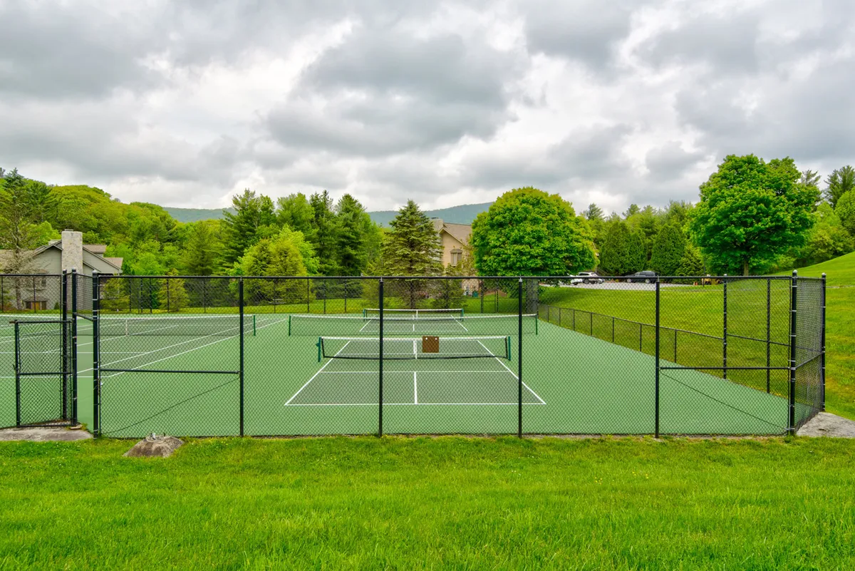 This image features tennis courts surrounded by lush greenery and distant hills. The setting is active and social, with the courts clearly visible as a hub for outdoor activities and gatherings. The vibrant outdoor scene highlights the resort's recreational offerings.