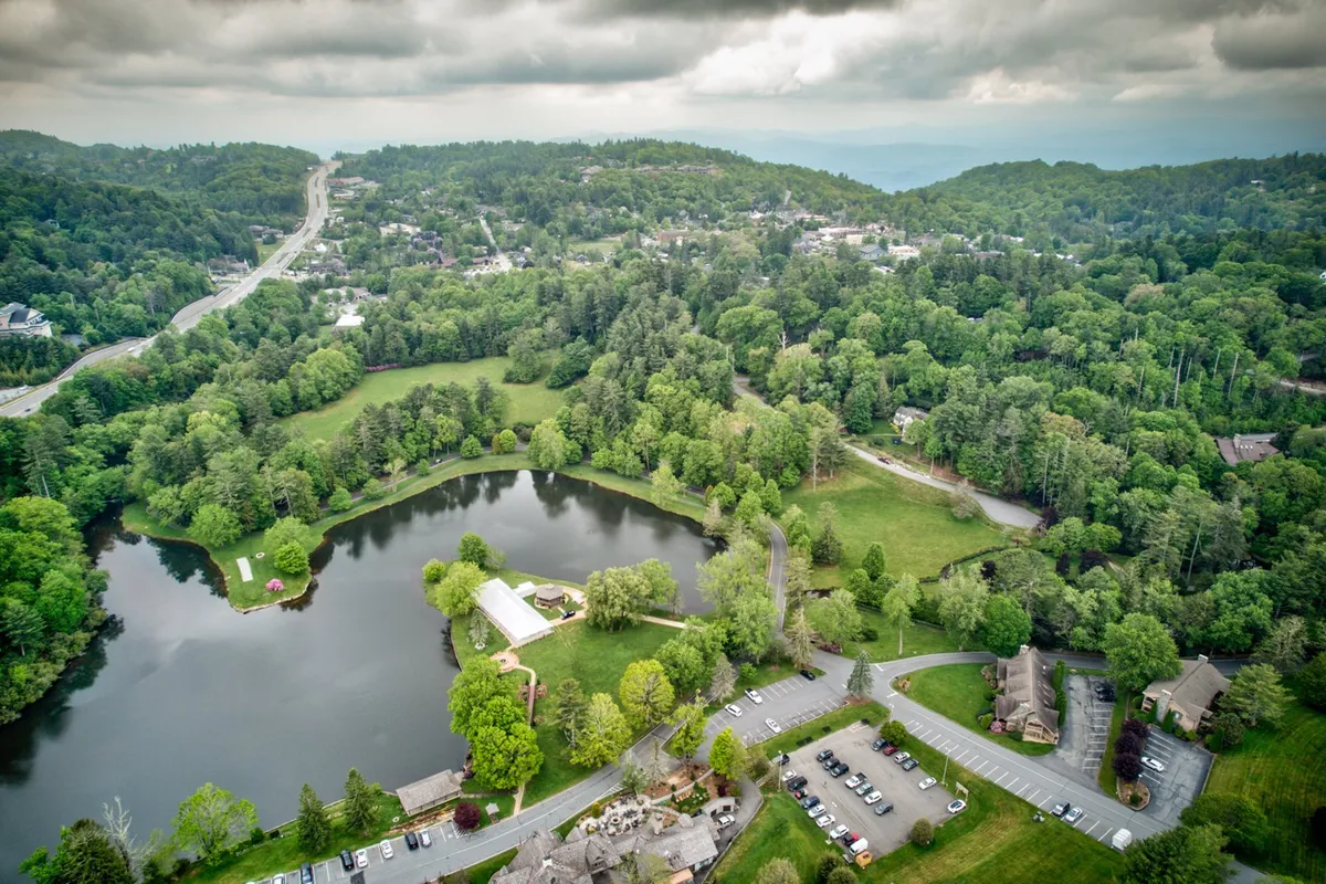 A peaceful lakeside scene with reflective water, green park space, and resort buildings in the background. The tranquil mood evokes relaxation and connection with nature, while suggesting a variety of outdoor activities available at the lake.