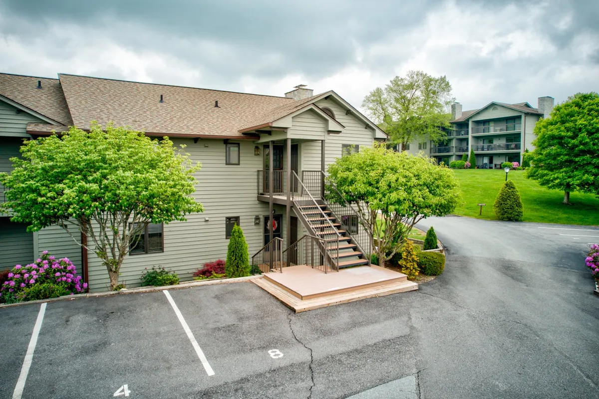This photo captures the staircase entry to the property, framed by green trees and flowering shrubs, with the parking area visible in the background. The inviting landscaping suggests a welcoming entry point and highlights the property's integration with the outdoors.