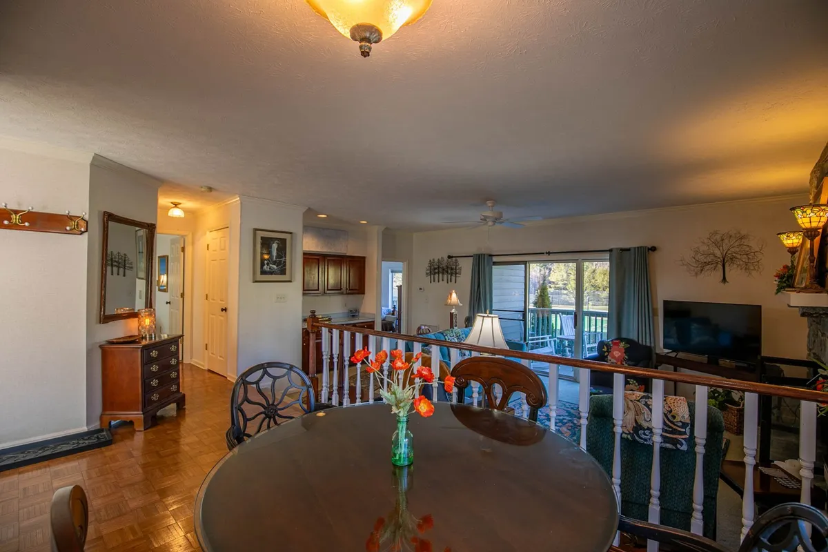 A cozy, inviting living and dining area featuring a beautifully set dining table with fresh flowers, a spacious living room with comfortable seating, and large windows with charming curtains that allow natural light to fill the space.