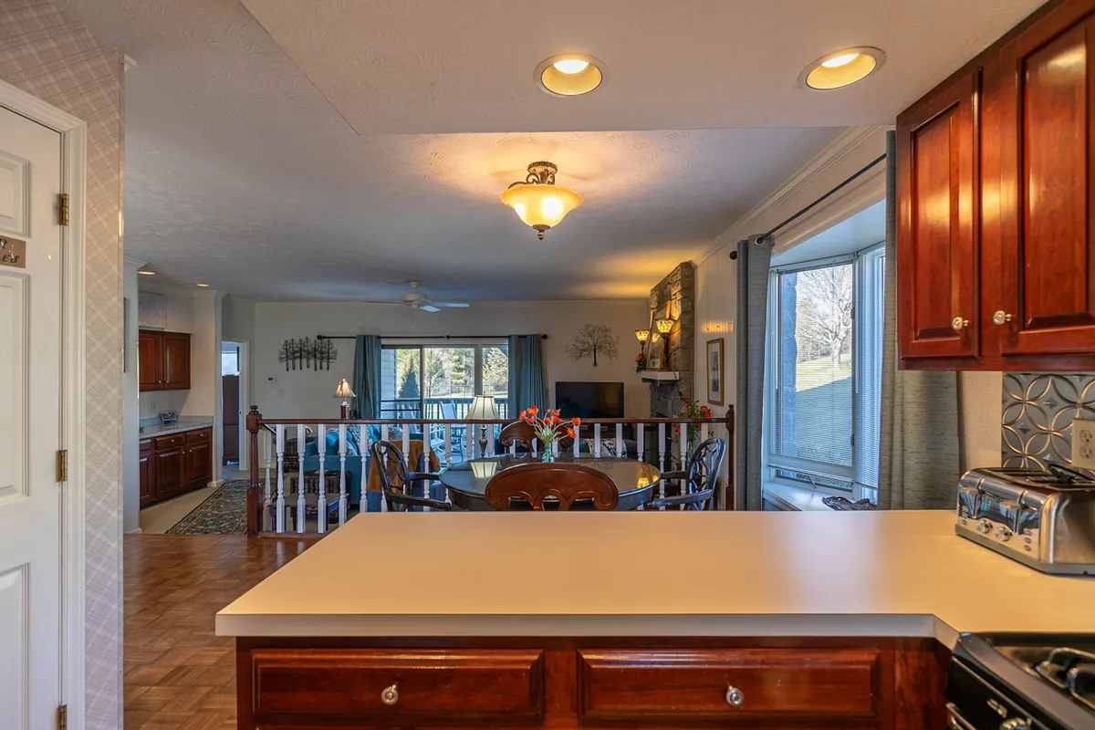 A wide shot of the condo’s inviting living and dining area, with sunlight streaming through a large window that offers a glimpse of the outdoors. The scene blends the kitchen’s gleaming countertop and a welcoming dining table, creating an environment perfect for unwinding and gathering together after a wellness activity.