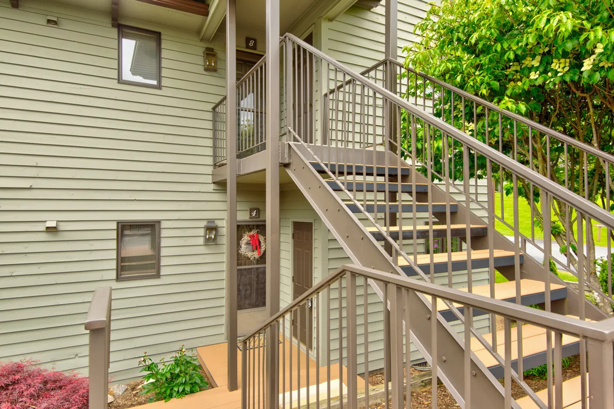 A charming exterior shot of the front entrance, framed with a green lawn, decorative wreath, and inviting staircase. The scene feels warm and welcoming, suggesting a cozy homecoming after a day of exploring together.