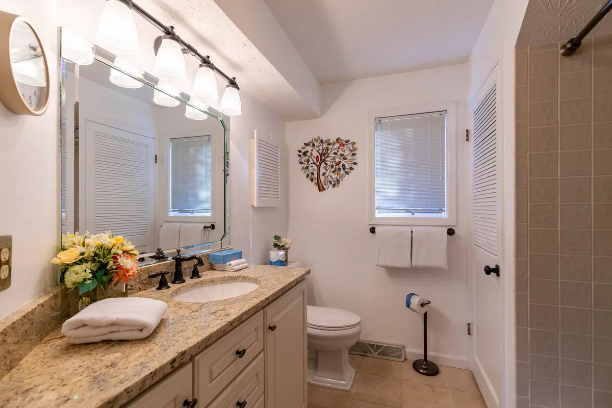 A stylish bathroom with a granite countertop, large lit mirror, and decorative floral touches. The space is designed for personal grooming and relaxation, with an inviting and tranquil ambiance.