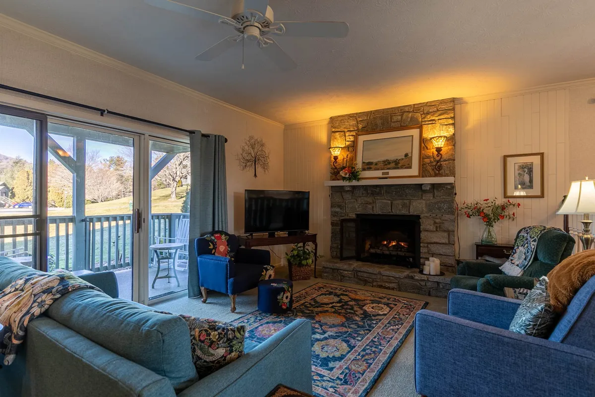 A warm, sunken living room with a plush sofa, armchair, and inviting rug arranged around a glowing fireplace. The setup is perfect for relaxing, socializing, or enjoying cozy evenings in. Large windows likely offer views beyond, enhancing the sense of connection to the outdoors.