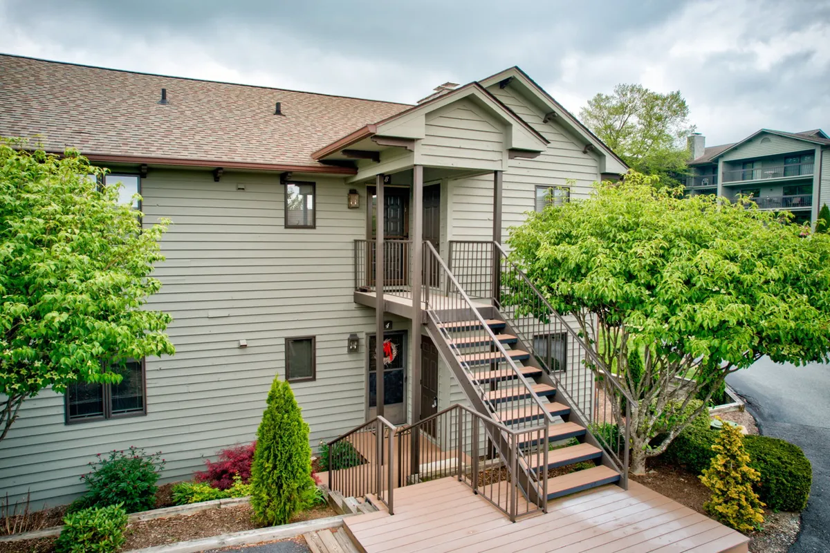 The image showcases the welcoming exterior of the Holly 4 condo at Chetola Resort. Visible are a charming staircase leading up to the front door, lush landscaping, and a cozy porch area—creating an inviting atmosphere that hints at relaxation and mountain getaways. Guests can easily imagine themselves approaching the entrance, enjoying the outdoor spaces, or gathering on the porch with friends and family.