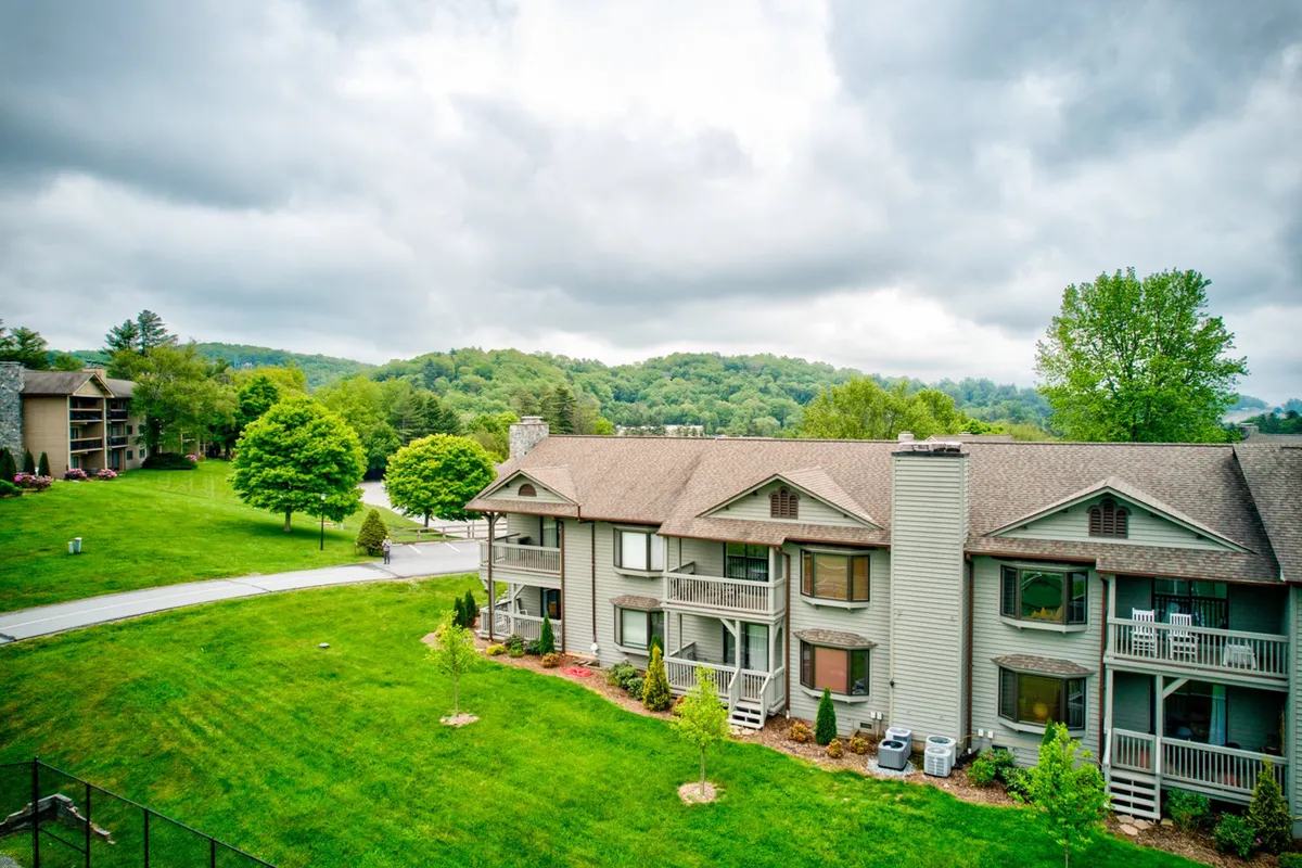 This exterior shot showcases the main apartment building surrounded by landscaped green spaces and a tranquil tree line. The scene highlights easy access to outdoor areas, suggesting room for walks, picnics, and safe family exploration all within the welcoming resort environment.