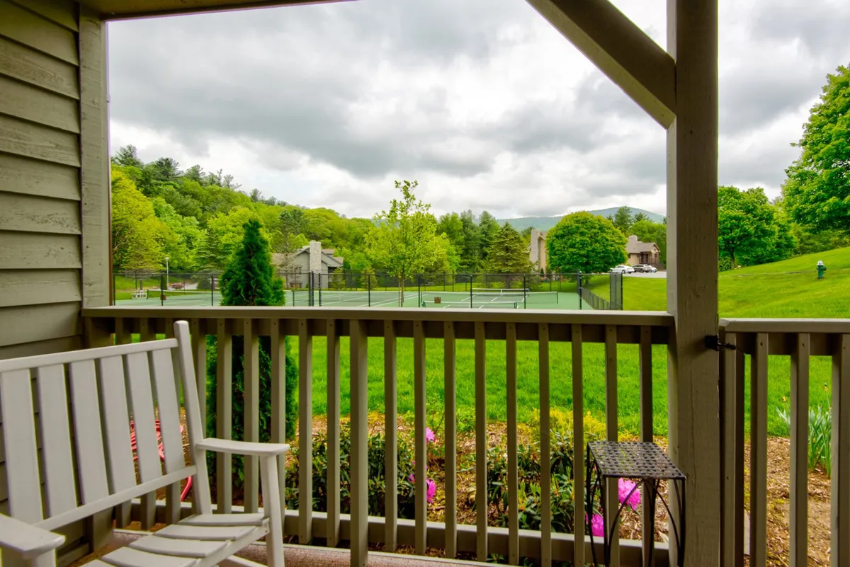 This view captures a wooden bench set on a lush green lawn, tennis courts, and a dramatic mountain backdrop. The space looks open, peaceful, and perfect for children to play or families to enjoy nature walks, with outdoor activities like tennis and casual family gatherings blending seamlessly into the natural surroundings.