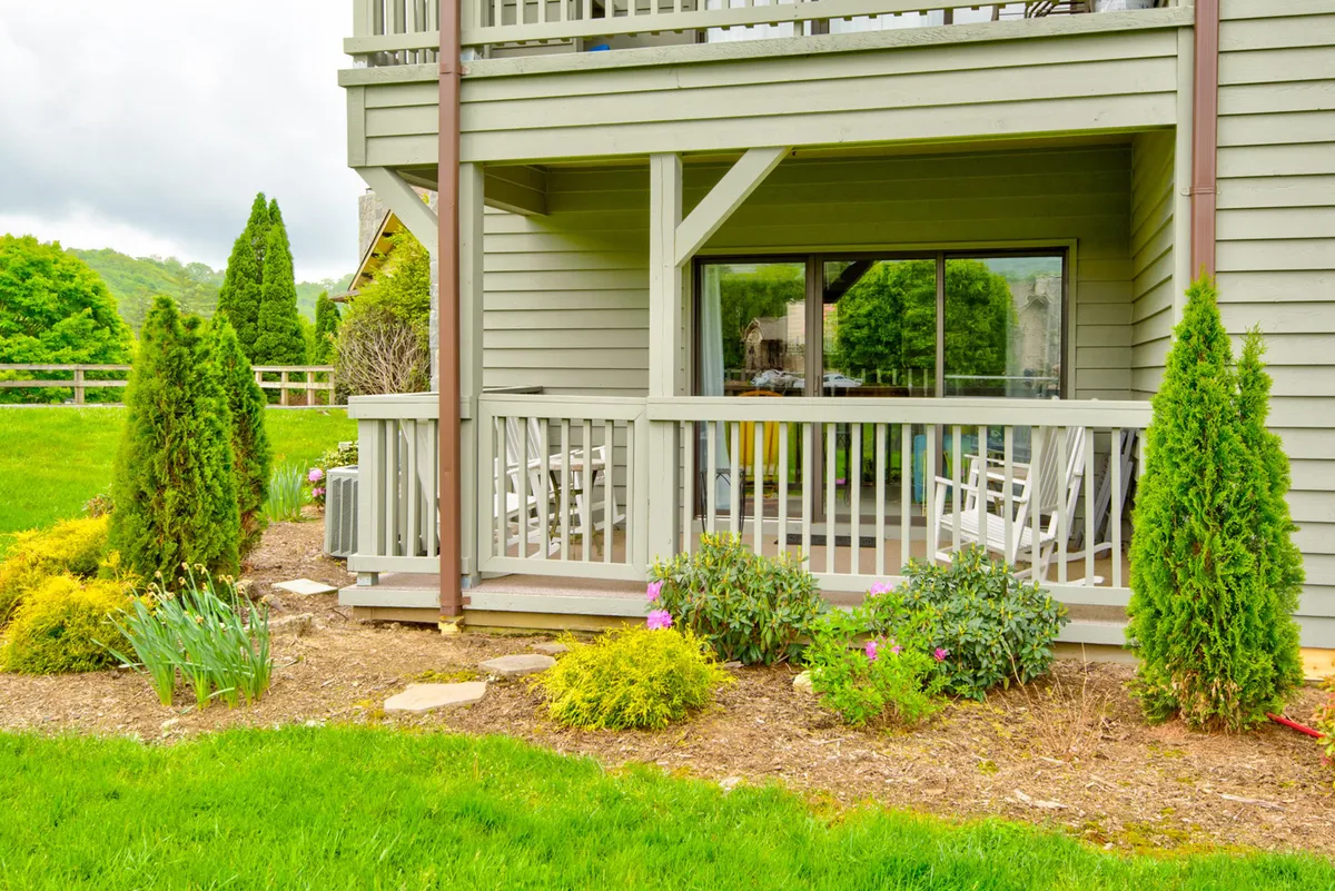 This image features a welcoming exterior scene with a balcony railing, outdoor seating, and vibrant flower beds. The area exudes a sense of relaxation and leisure, suggesting a sunny, safe, and social place for families to gather and unwind. Children can be imagined playing nearby, while adults relax and enjoy the fresh mountain air.
