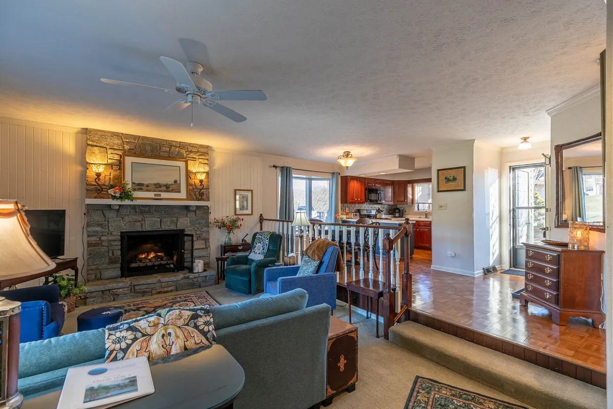 An inviting open-plan living space featuring a stone fireplace, plush sofa, and a stylish kitchen area—all arranged for comfort, conversation, and entertaining guests.