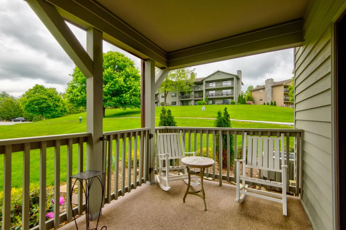 A tranquil balcony scene with two classic rocking chairs and a small round table overlooking lush greenery. The landscape beyond suggests a peaceful retreat, perfect for couples wishing to enjoy quiet moments or scenic sunsets together.